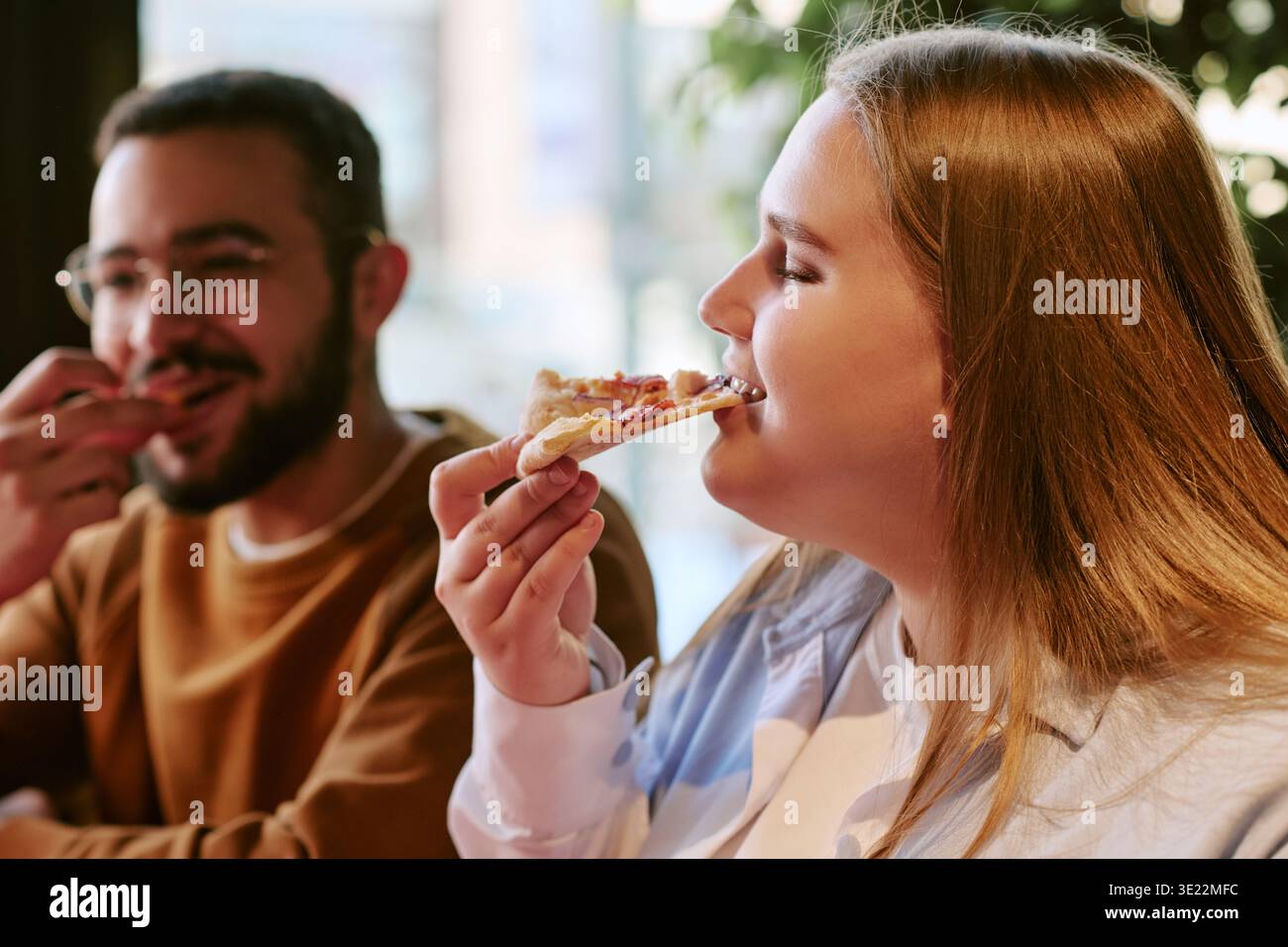 Eine junge Frau genießt Pizza mit einem jungen Mann drinnen Stockfoto