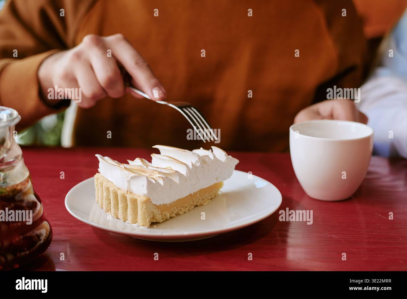 Junger Erwachsener, der Kuchen isst und Kaffee am Cafe Table trinkt Stockfoto