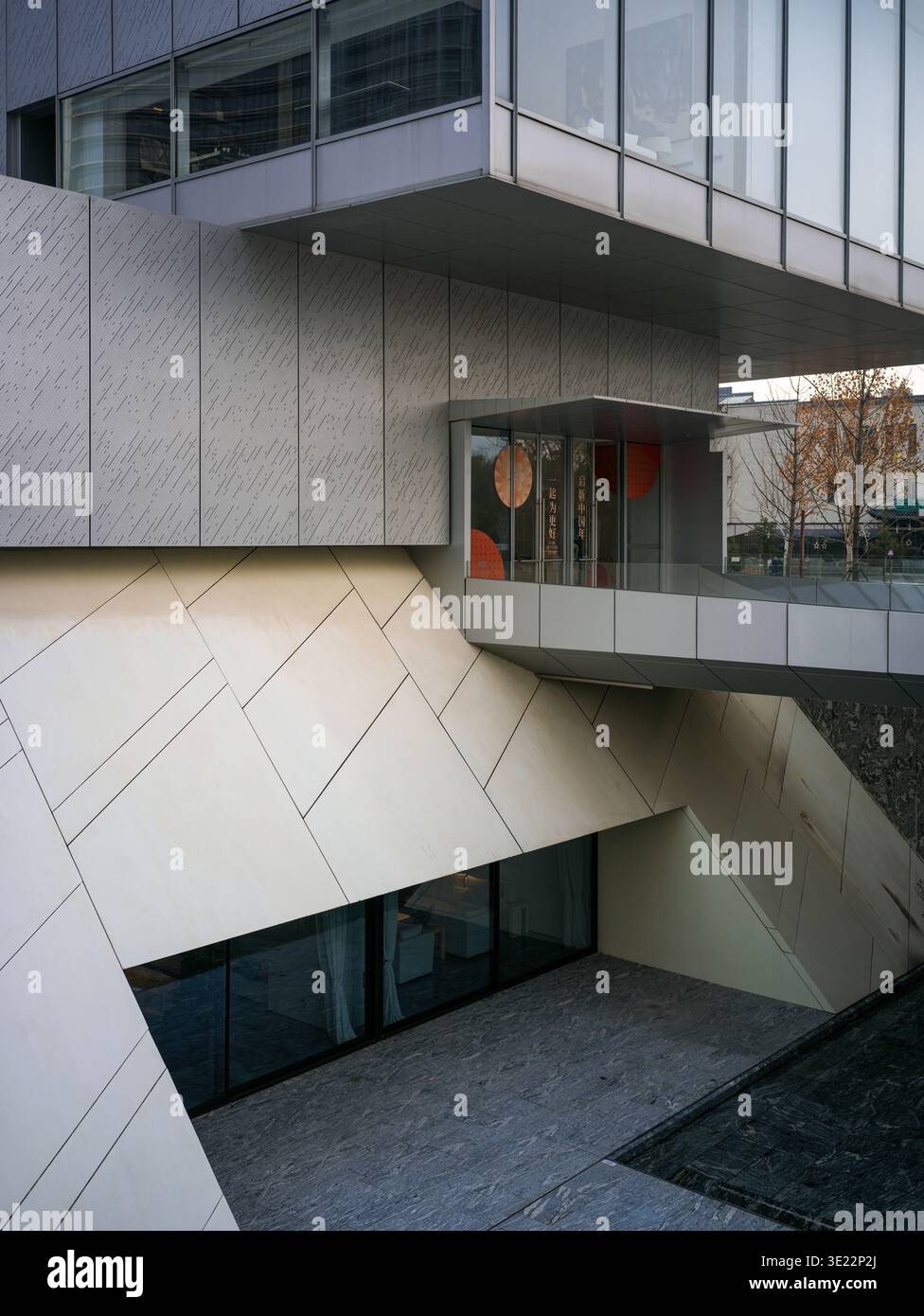 Blick auf einen modernen Gebäudekomplex mit diagonalen architektonischen Linien, Steinverkleidungen, Glasfassaden und einem strukturierten eingelassenen Innenhof. Re Stockfoto