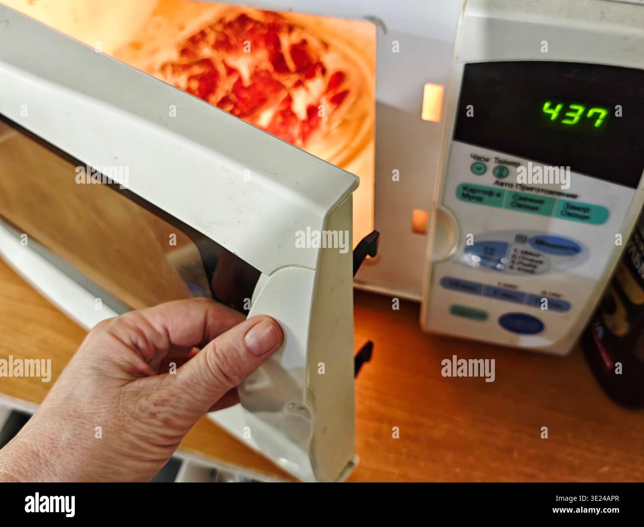 Eine Person öffnet die Tür eines Mikrowellenherds, um Lebensmittel in einer Küche zu erhitzen. Auf dem Display wird der Timer deutlich angezeigt. Stockfoto