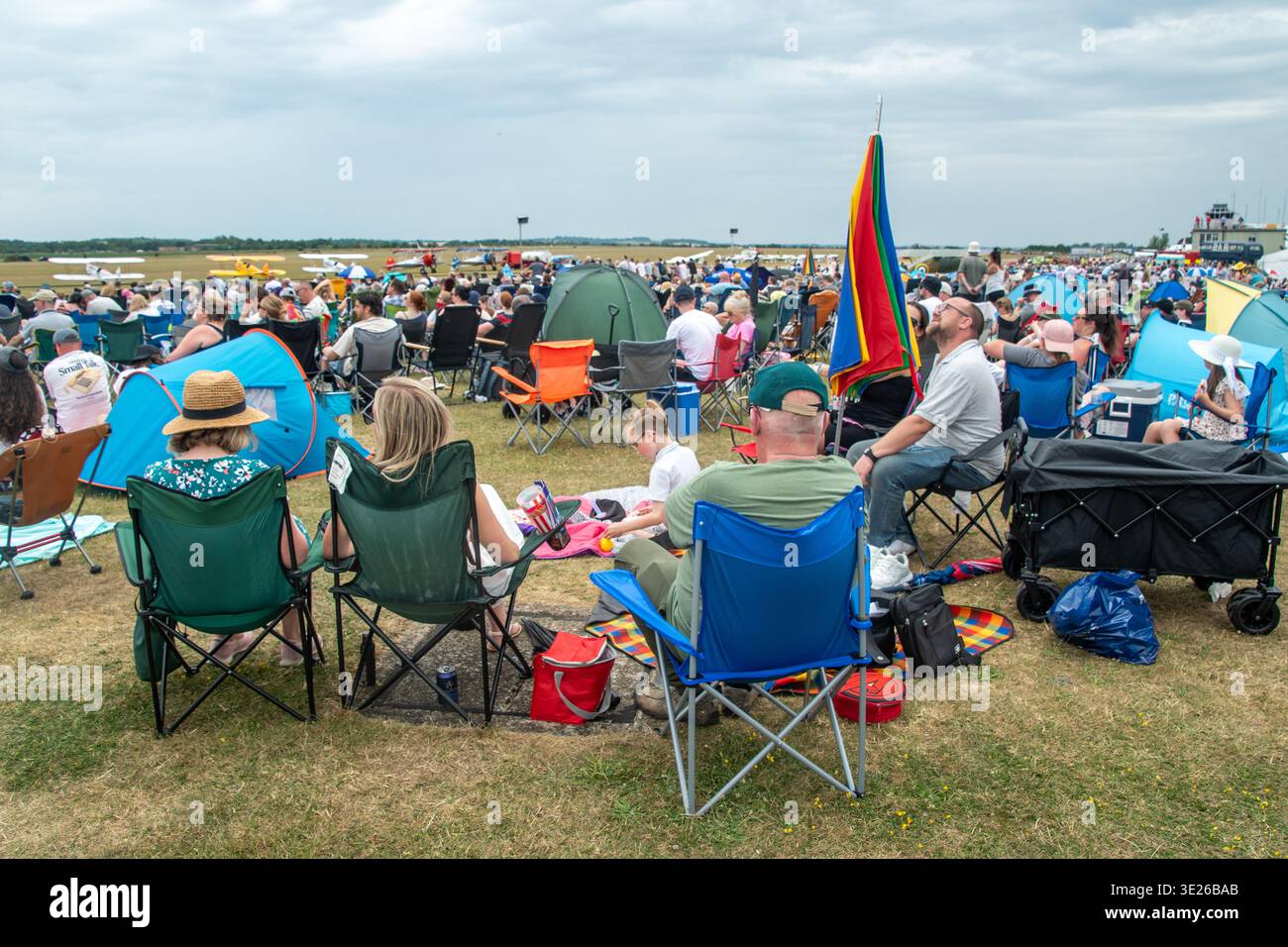 IWM Duxford Summer Airshow - Hunderte von Zuschauern sitzen auf Klappstühlen und Picknickdecken bei einer Flugschau auf dem Flugplatz und beobachten dabei kleine Flugzeuge. Stockfoto
