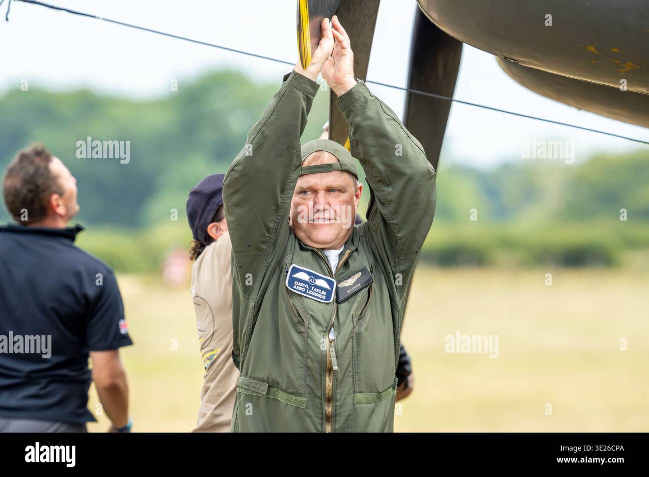 Headcorn Battle of Britain Airshow – ein lächelnder Pilot in grünem Fluganzug greift nach oben, um ein Oldtimer-Flugzeug bei einer Outdoor-Airshow auf einem offenen AirFi zu sichern Stockfoto