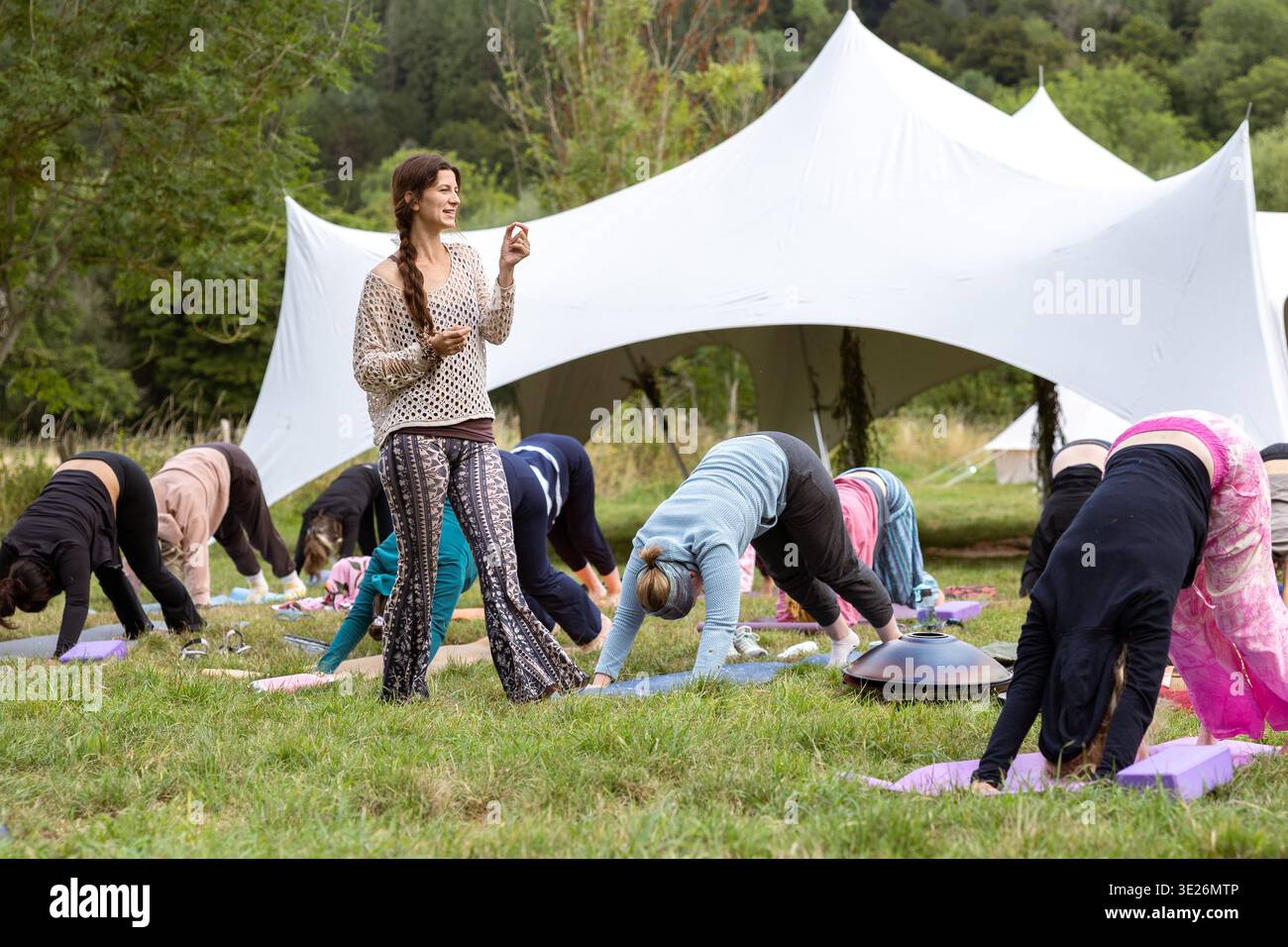Lehrerin, die eine Gruppe von Frauen anführt, die im Freien auf Yogamatten posieren Stockfoto