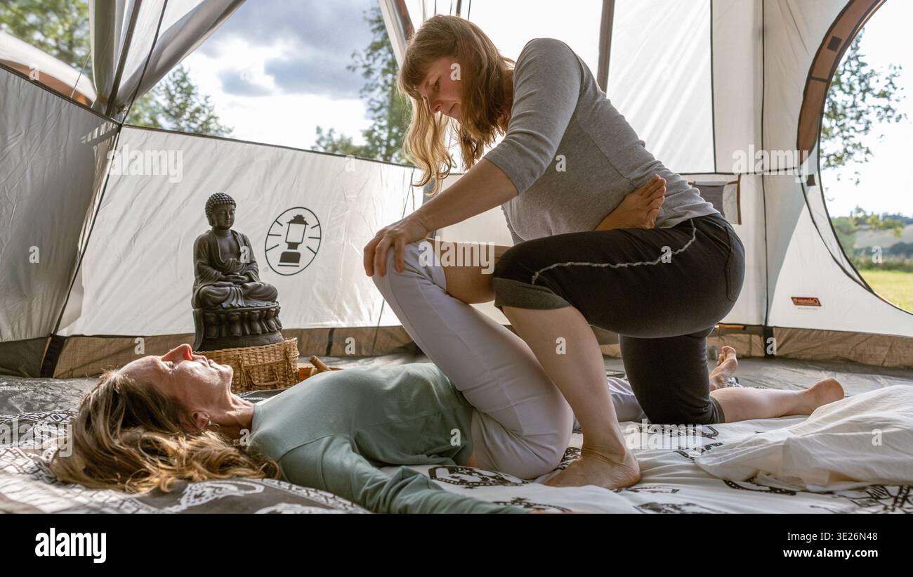 Frau, die traditionelle thai-Massage mit Dehnung auf einer anderen Frau in einem Außenzelt durchführt Stockfoto