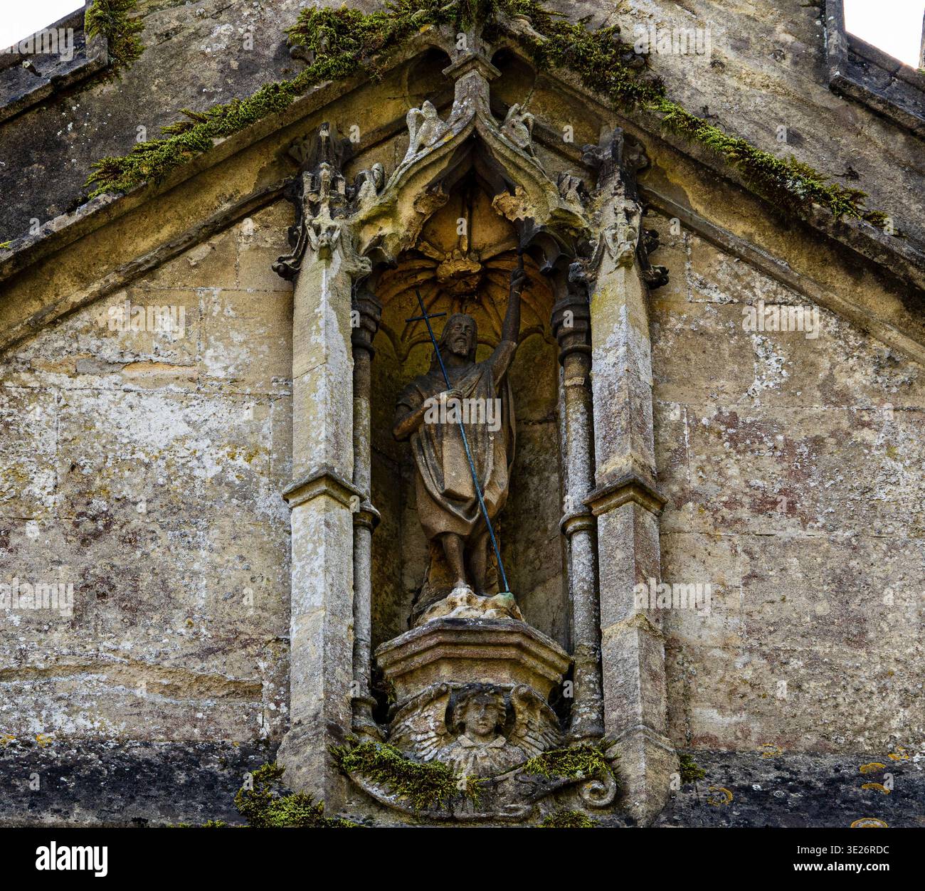 Steinstatue eines heiligen mit einem Kreuz in einer reich verzierten gotischen Architekturnische an einer alten verwitterten Kirchenfassade St. John the Baptist Pewsey Wilts Stockfoto