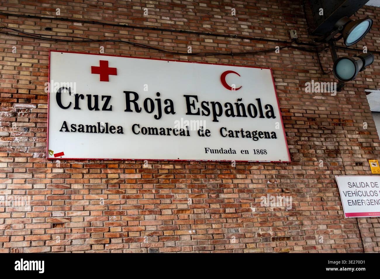 Hauptquartier des spanischen Roten Kreuzes in Cartagena, Spanien, mit einer Ziegelfassade mit Beschilderung für die lokale Versammlung und einem Notfahrzeug-Ausstiegsschild. Stockfoto