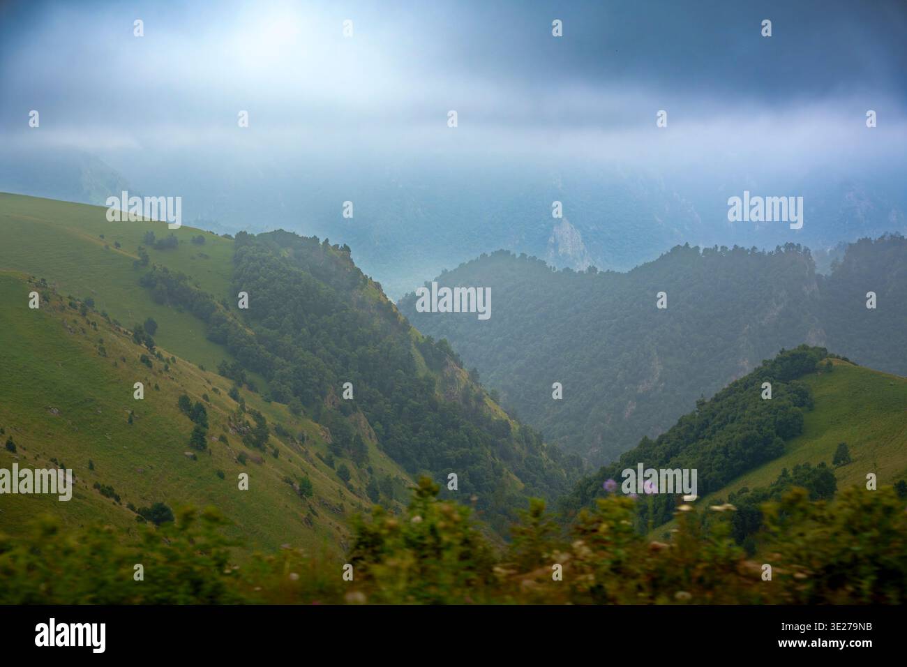Malerisches Bergtal mit grünen Graten und dramatischem bewölktem Himmel. Stimmungsvolle Sommerlandschaft mit weichem Dunst, Sonnenlicht auf den Hügeln und weitläufigem na Stockfoto