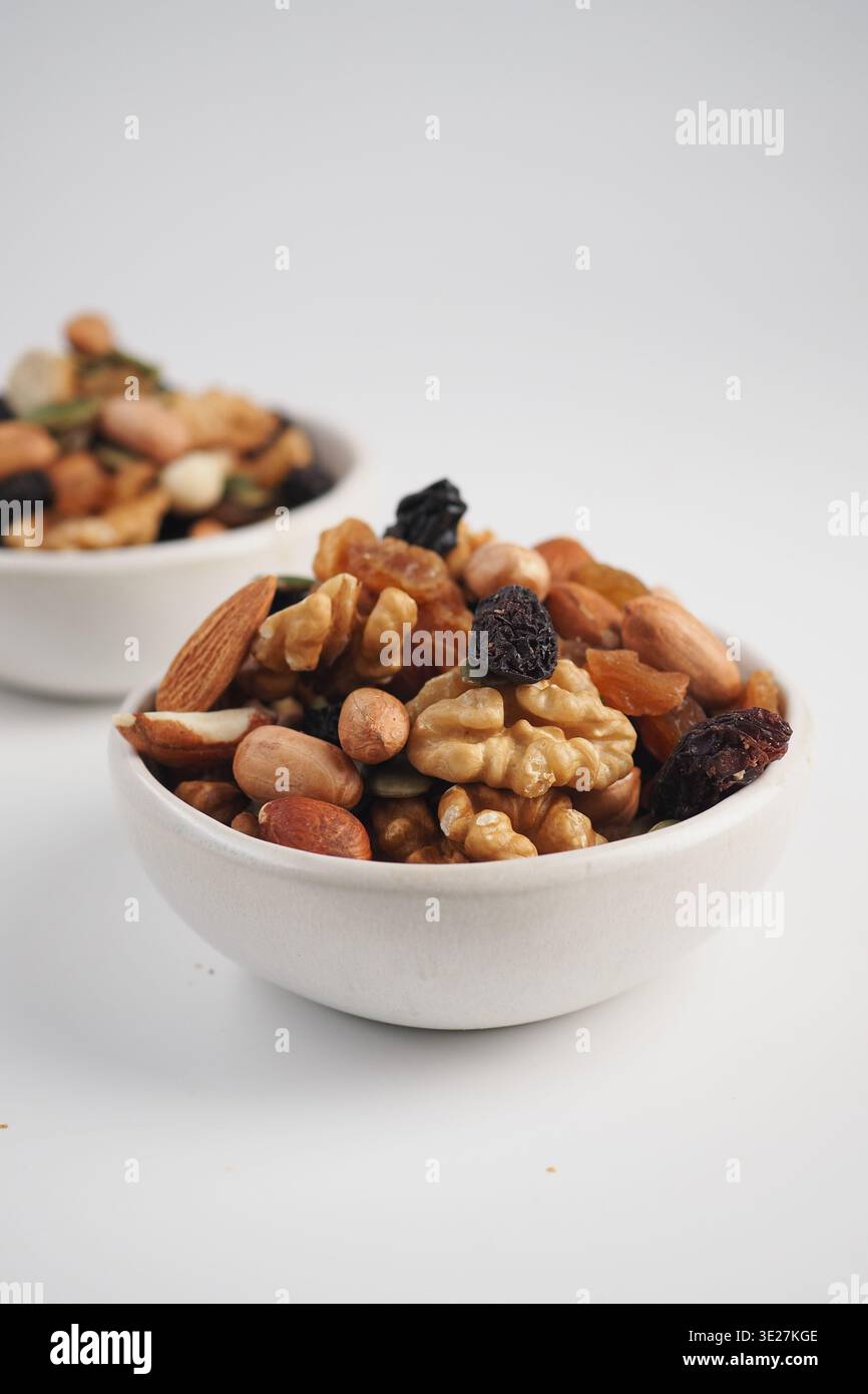 Nüsse und getrocknete Früchte mischen sich in weißen Schüsseln auf einer hellen Oberfläche Stockfoto