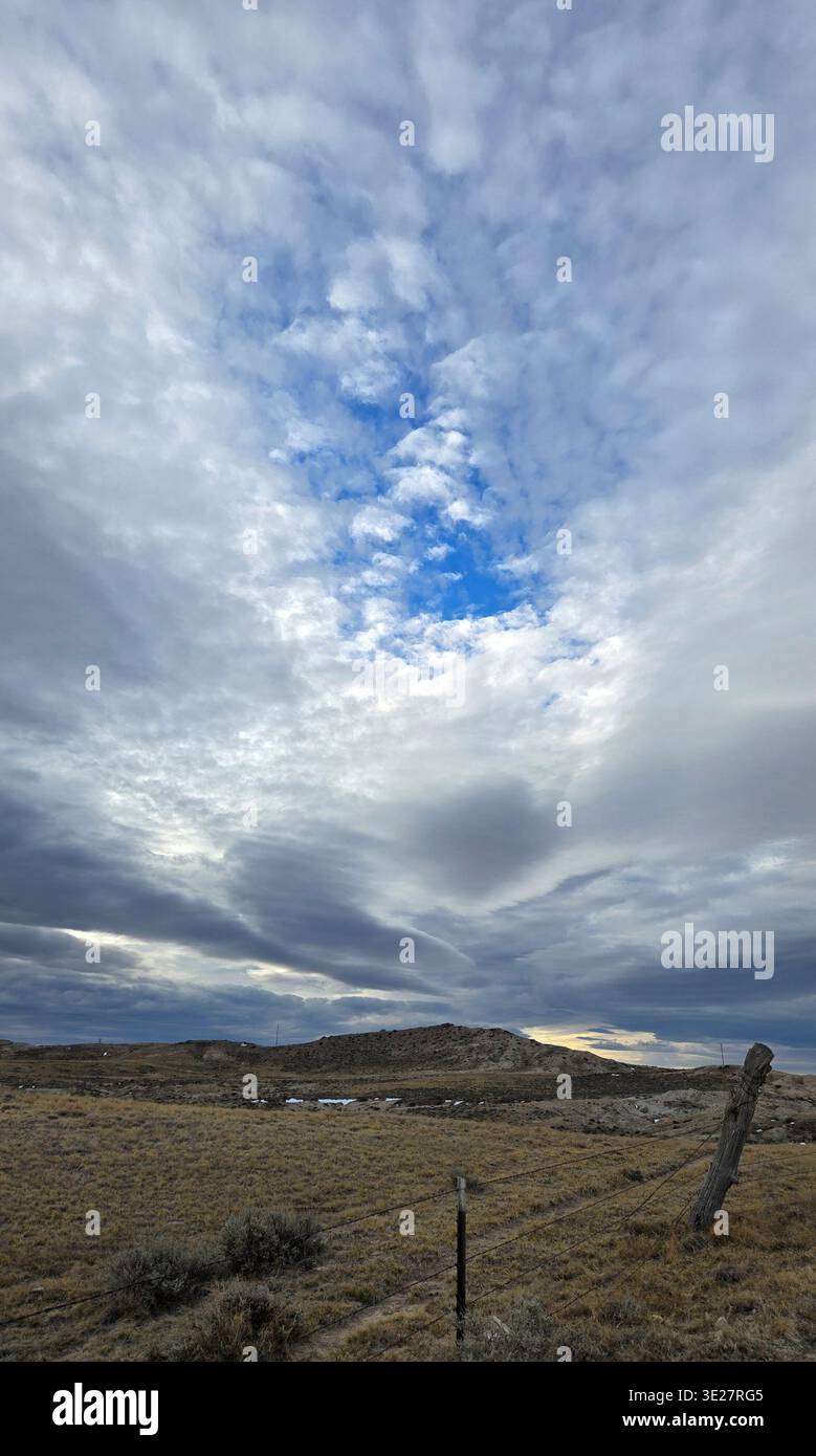 Blau öffnet sich an einem bewölkten Nachmittag ein bisschen in Wolken. Unter den Wolken, im ländlichen Wyoming, hat diese Weide im Winter 2026 trockenes Wildgras. Stockfoto