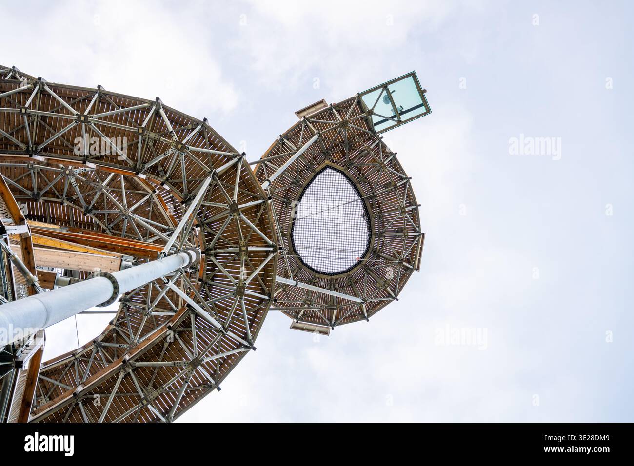 Besucher stehen unter einem großen Holzbau mit kreisförmigem Design. Er reicht hoch in den Himmel und zeigt einen vernetzten Bereich darüber. Der Himmel ist bewölkt und die Szene ist sehr beschäftigt. Stockfoto