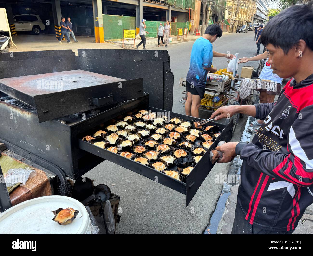 Philippinischer Straßenverkäufer, der traditionelle Bibingka-Reiskuchen im Holzkohleofen an der Straße backt, Cebu City Philippines, lokale Street Food-Szene - Smartphone-aufgenommenes Stockfoto