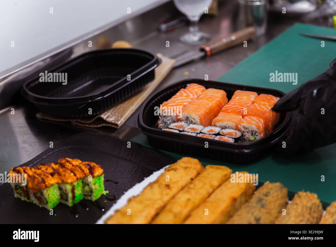 Verschiedene Sushi- Und Gebratene Rolls Zum Mitnehmen Im Black Container, Koch Bereitet Ausgewogen Vor Stockfoto