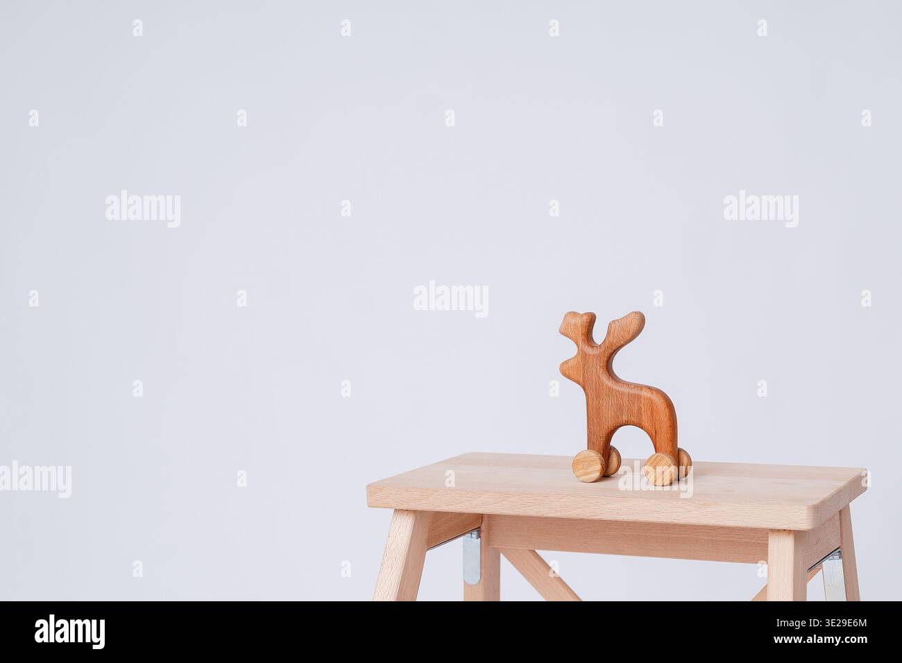 Minimales Banner mit Holzhirsch Spielzeug auf Rädern auf dem Hocker vor sauberem Hintergrund. Großer Kopierbereich rechts für Text, Werbung und Branding Stockfoto