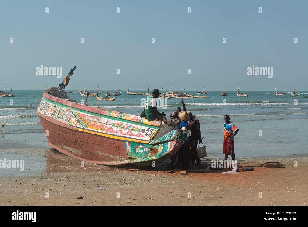 Eine kleine Gruppe von Fischern auf der Rückseite eines hölzernen Fischerbootes (Pirogue) am Strand von Kafountine bei Ebbe. Senegal Stockfoto