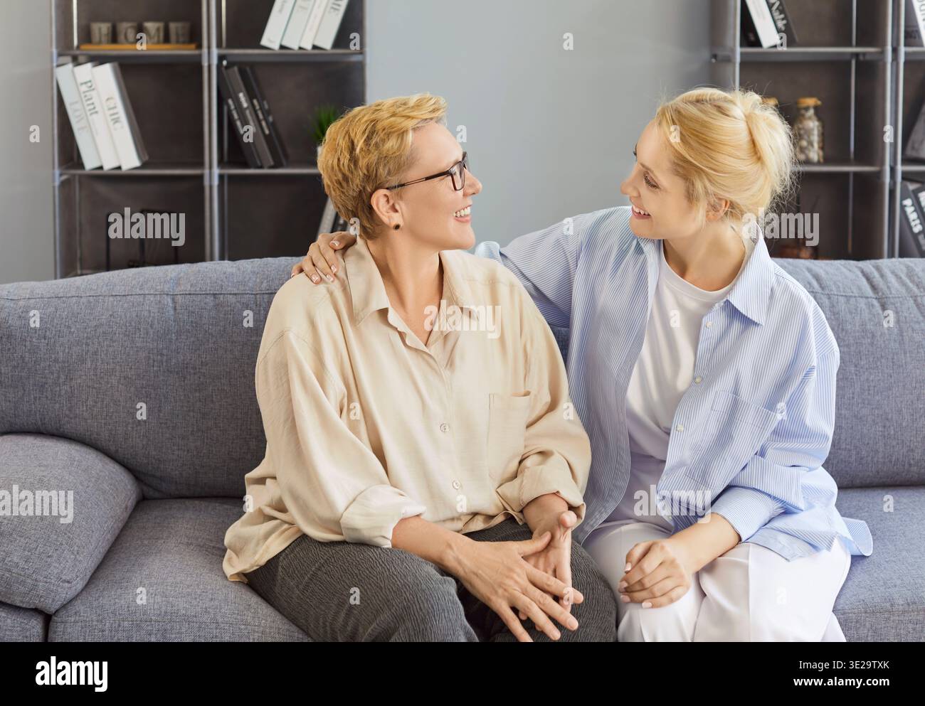 Glückliche Seniorenmutter und Erwachsene Tochter sitzen zu Hause auf dem Sofa, freundliche Frauen lächeln herzlich Stockfoto