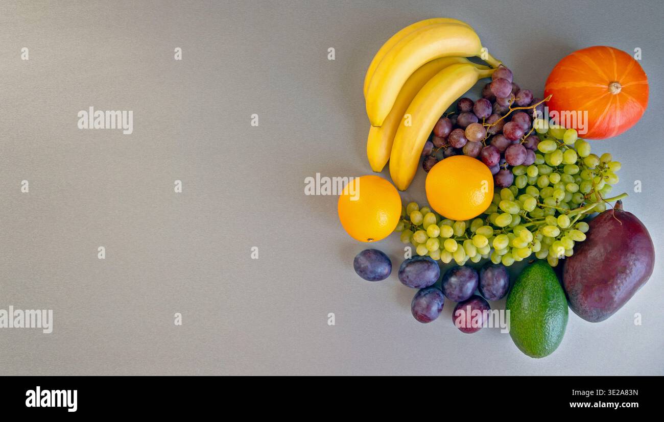 Eine bunte Auswahl an Früchten mit Kürbis auf grauem Hintergrund. Eine lebendige Präsentation von frischem Obst, einschließlich Bananen, Trauben, Orangen, Pflaumen, Avocado Stockfoto