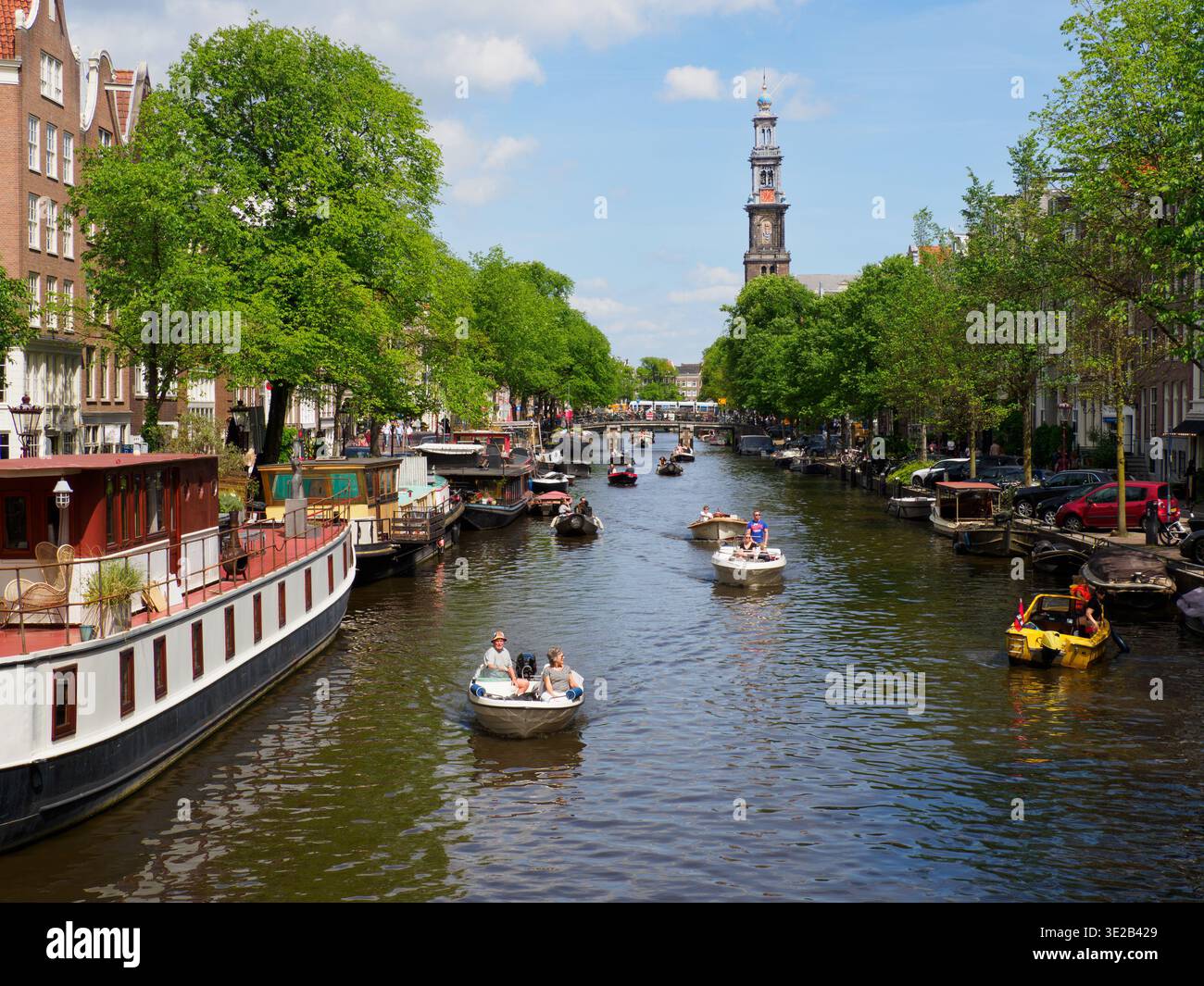 Touristen segeln einen Kanal an einem sonnigen Nachmittag in Amsterdam, Holland, mit traditionellen Booten und historischer Backsteinarchitektur und der Wester Ke Stockfoto