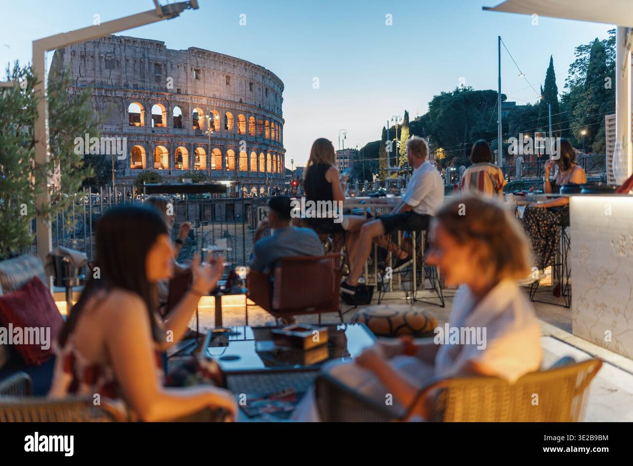 Nicht erkennbare Leute genießen Drinks mit Blick auf das Kolosseum in Rom in der Abenddämmerung. Stockfoto
