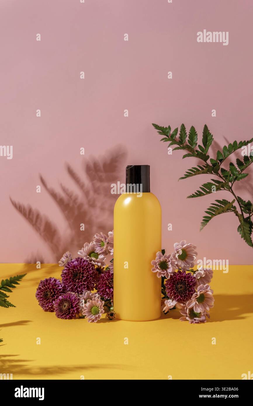 Sommerstil der Präsentation von Kosmetikprodukten auf gelbem und pinkfarbenem Hintergrund mit Blumen. Gelbe Flasche Kosmetikprodukt mit Blumen Stockfoto