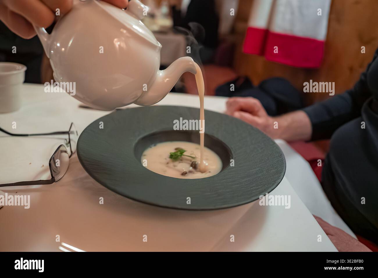 Der Koch gießt im Alpenrestaurant Oberlech cremige Suppe in eine Schieferschale Stockfoto
