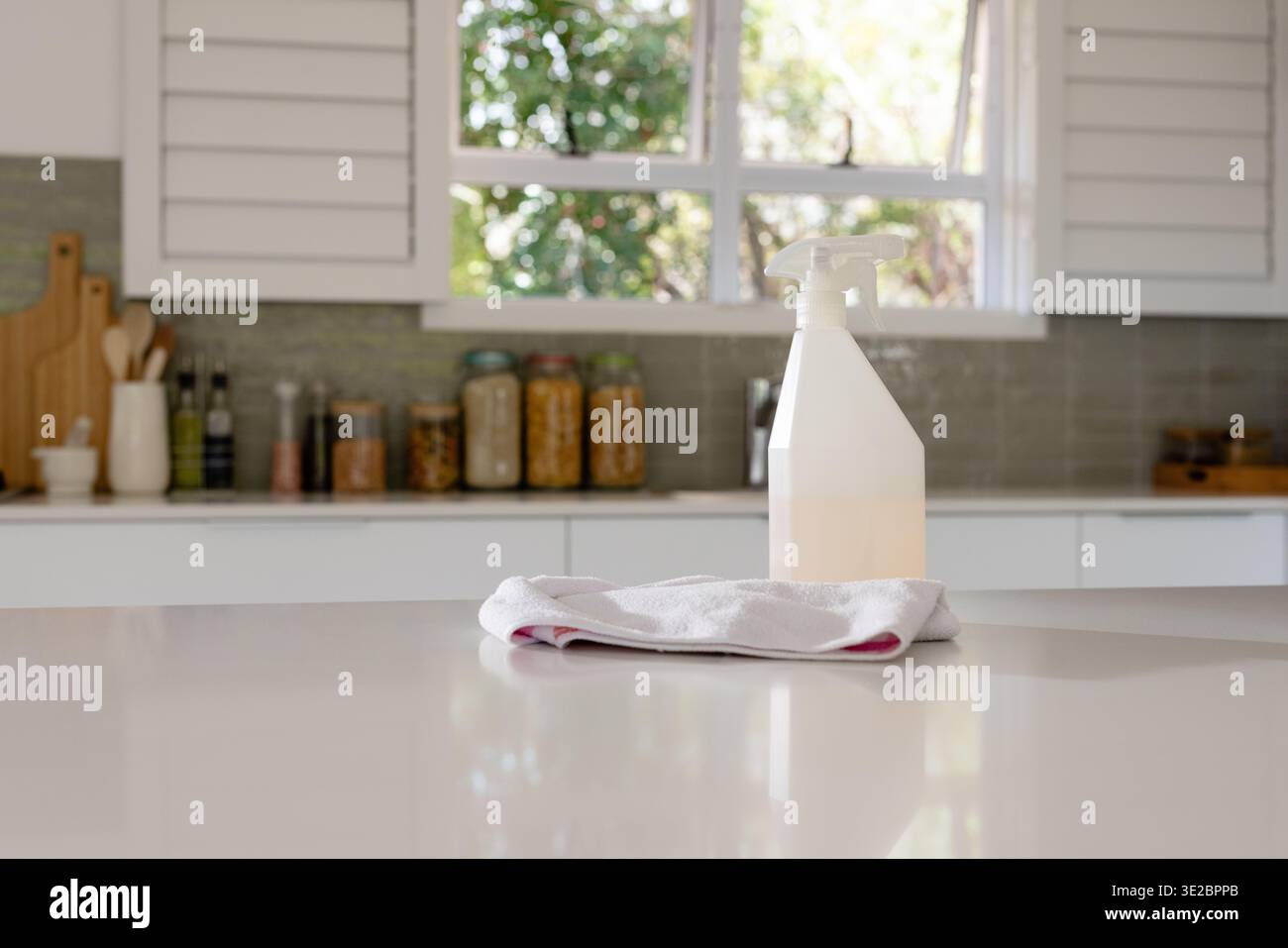 Sprühflasche mit Flüssigkeit auf Mikrofasertuch auf Küchenarbeitsplatte mit Pantry-Gläsern. Sprühgerät, Lösung, Behälter, Rückspritzer, Taglig Stockfoto