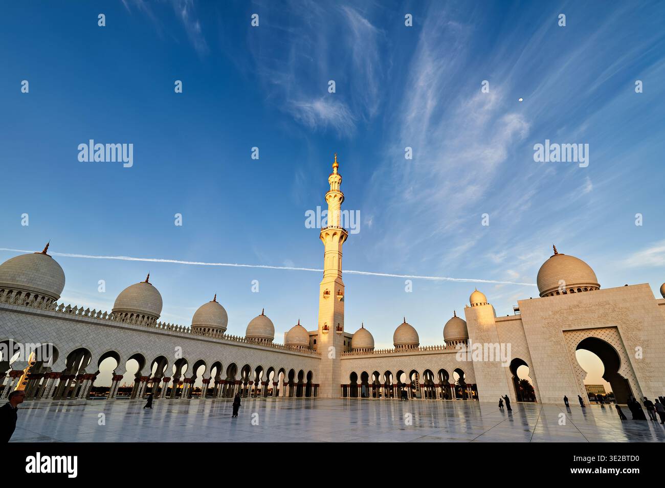 Während des Sonnenuntergangs spazieren die Menschen um die Scheich-Zayed-Moschee in Abu Dhabi. Die Moschee zeigt ihre architektonische Schönheit und Pracht. Stockfoto