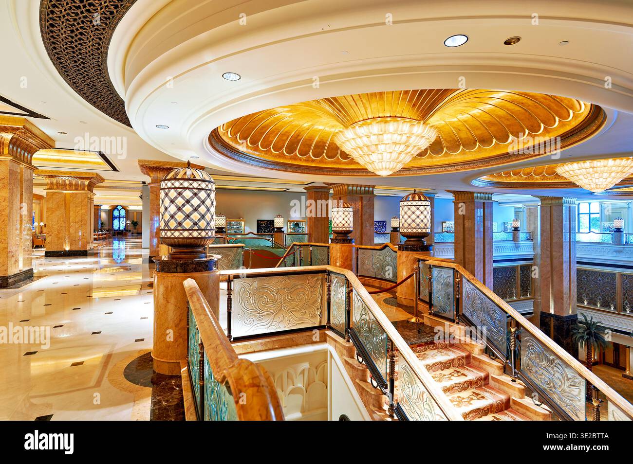 Gäste laufen durch die Halle des Emirates Palace Hotel in Abu Dhabi. Der Innenraum zeigt kunstvolle Details und helle Beleuchtung im gesamten Raum. Stockfoto
