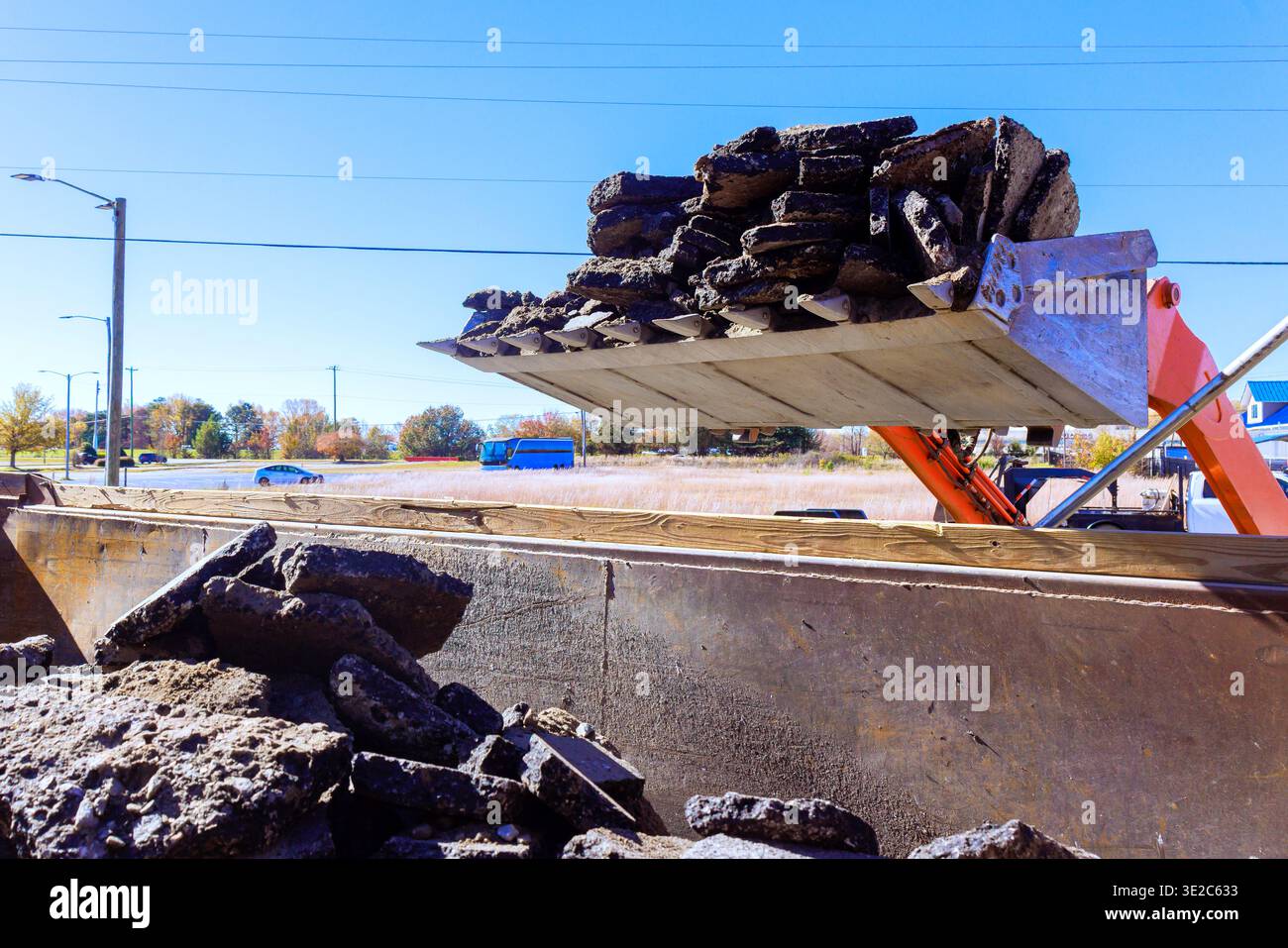 Das Baufahrzeug entlädt Asphaltabfälle in Müllcontainer in der Nähe von stark befahrenen Straßen in der Stadt Stockfoto