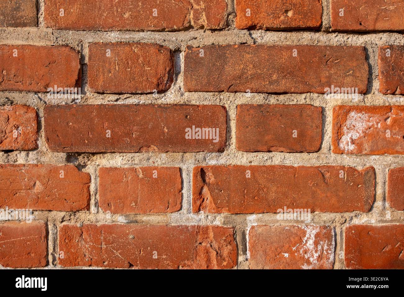 Nahaufnahme einer strukturierten roten Ziegelmauer mit Mörtelfugen, die die natürlichen Variationen und Mängel der Ziegelsteine zeigt Stockfoto