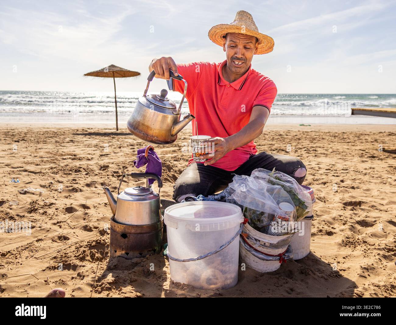 Traditioneller marokkanischer Teehändler, der Minztee am Strand in Taghazout in der Nähe von Agadir, Marokko, gießt Stockfoto