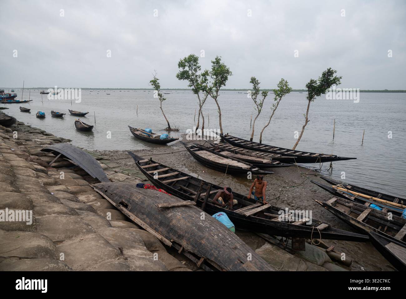 Satkhira, Bangladesch - 25. April 2025: Blick auf verwitterte Holzboote ruhen auf dem matschigen Ufer, im Kontrast zum grauen Himmel und fernen Horizont. Stockfoto