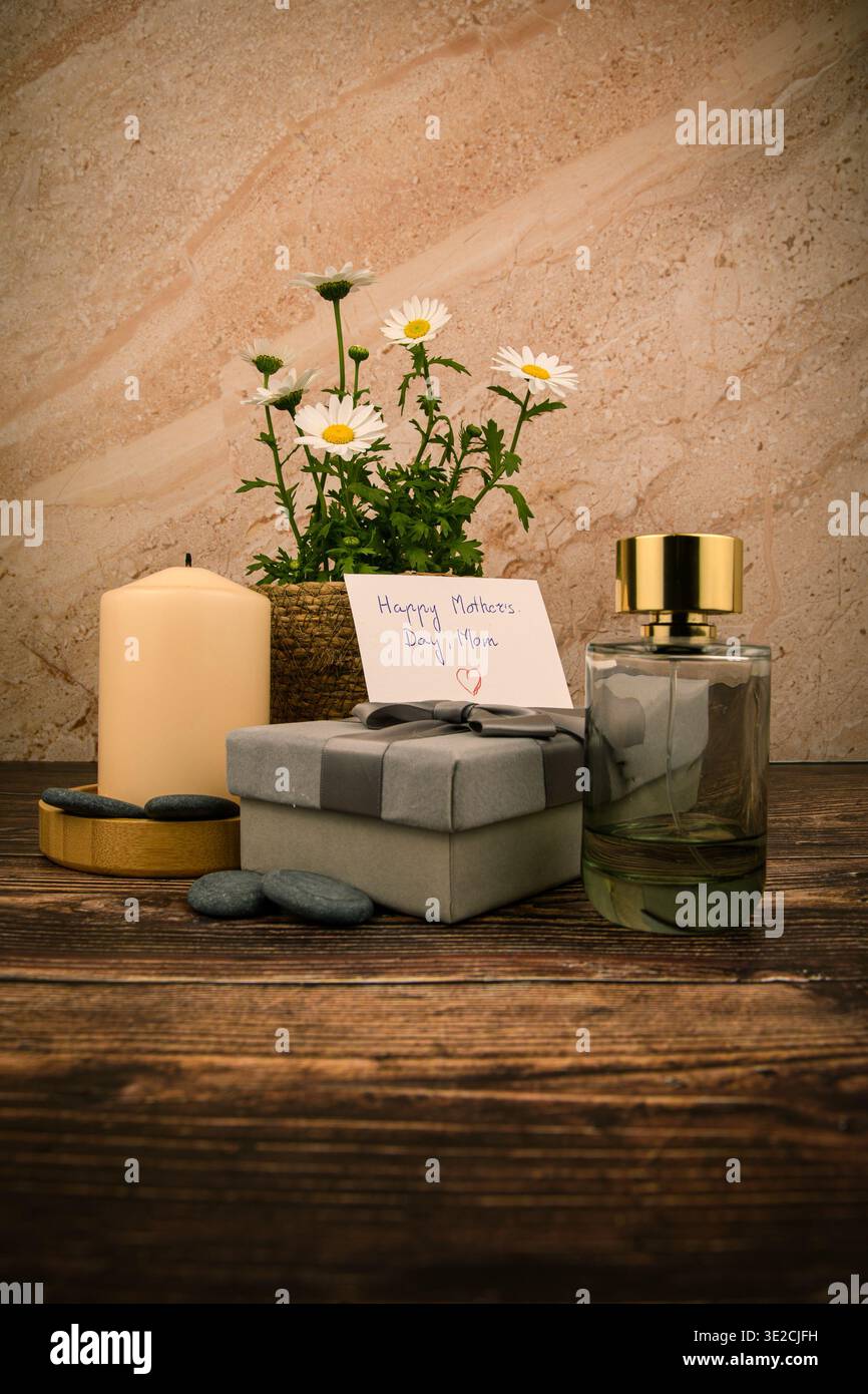Stillleben zum Muttertag mit Gänseblümchen, handgeschriebener Karte, Kerze, Parfümflasche und verpacktem Geschenk auf rustikalem Holz, gestaltet für Spa, Schönheit und Feier Stockfoto