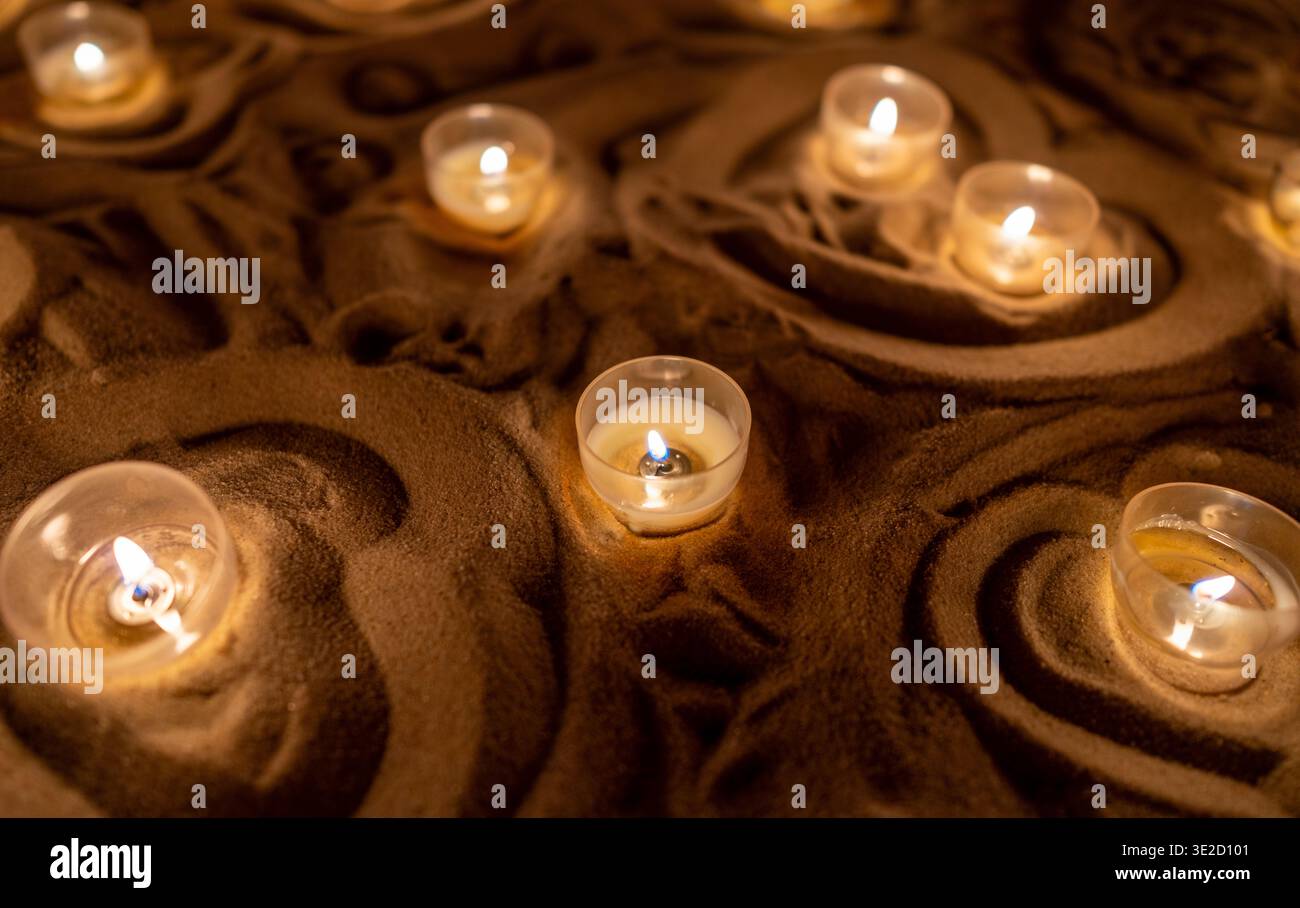 Kleine Teelichterkerzen leuchten in dekorativen Sandwirbeln und schaffen eine warme Spa-Atmosphäre mit weichem Bokeh und ruhigem Umgebungslicht für Entspannung Stockfoto
