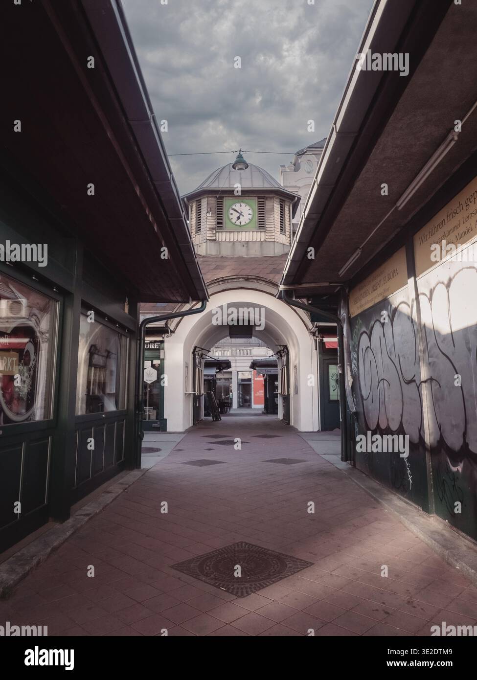 Naschmarkt Vienna Passage: Überdachte Arkade mit Uhrenturm, Graffiti-Wänden und Markteingang, bewölkter Himmel darüber. Stockfoto