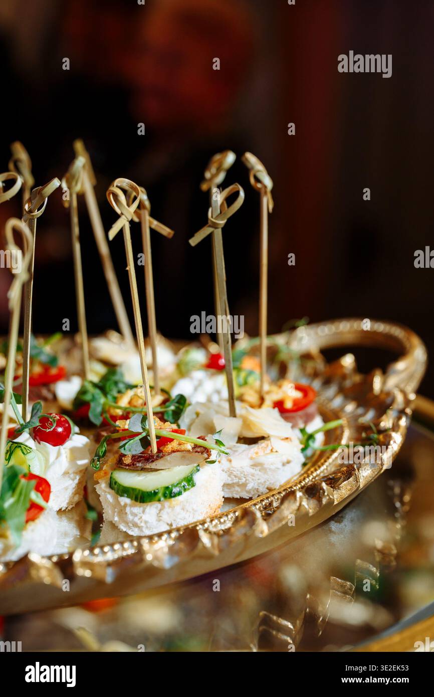 Nahaufnahme einer luxuriösen goldenen Platte mit eleganten Häppchen mit Frischkäse, Gurkenscheiben, Kirschtomaten, Kräutern, Nüssen und künstlerischem Ba Stockfoto