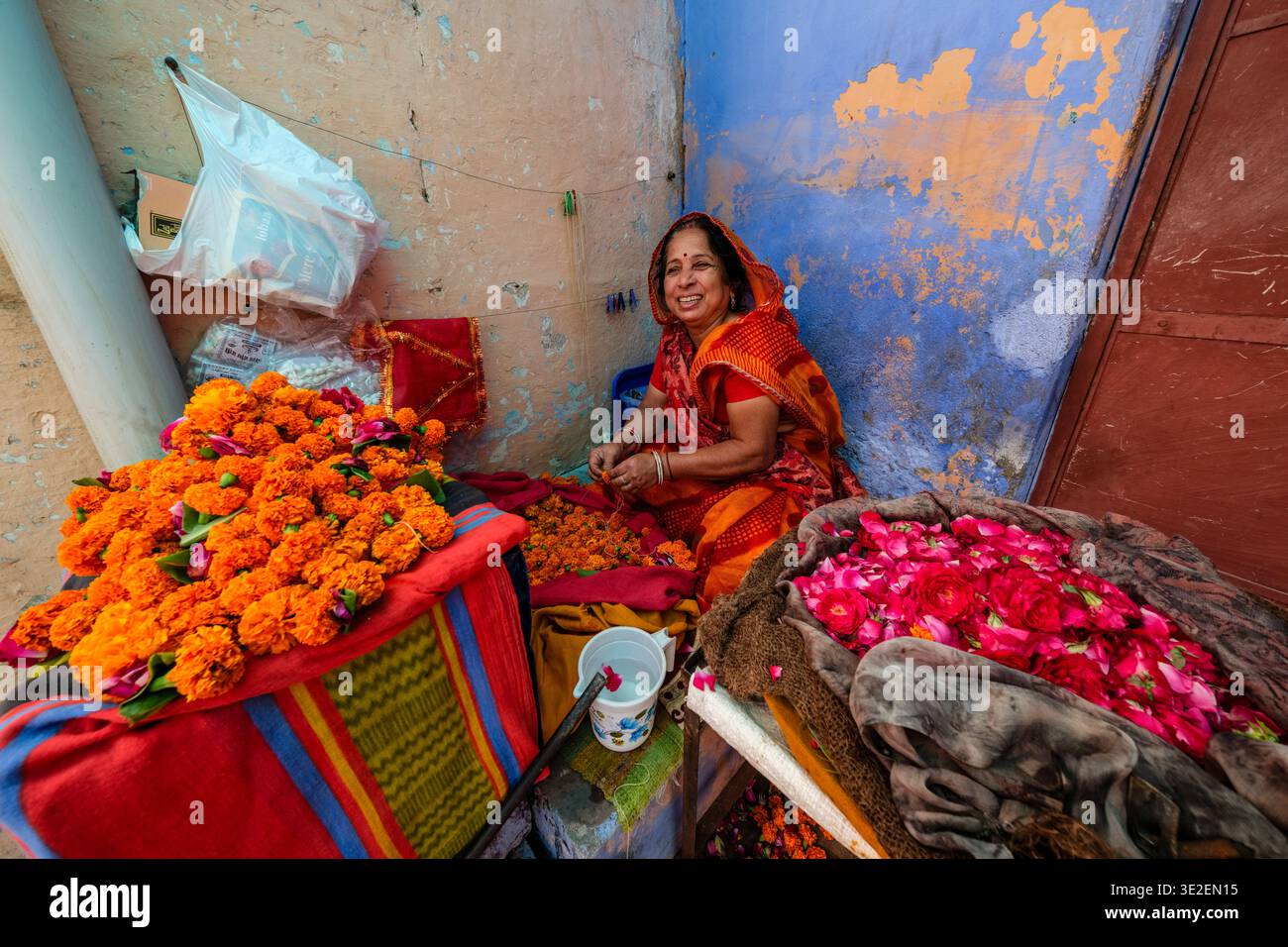 Eine lächelnde Frau in Bundi sitzt auf dem Boden und bereitet lebendige Ringelblumen- und Rosengirlanden für lokale religiöse Zeremonien vor. Stockfoto