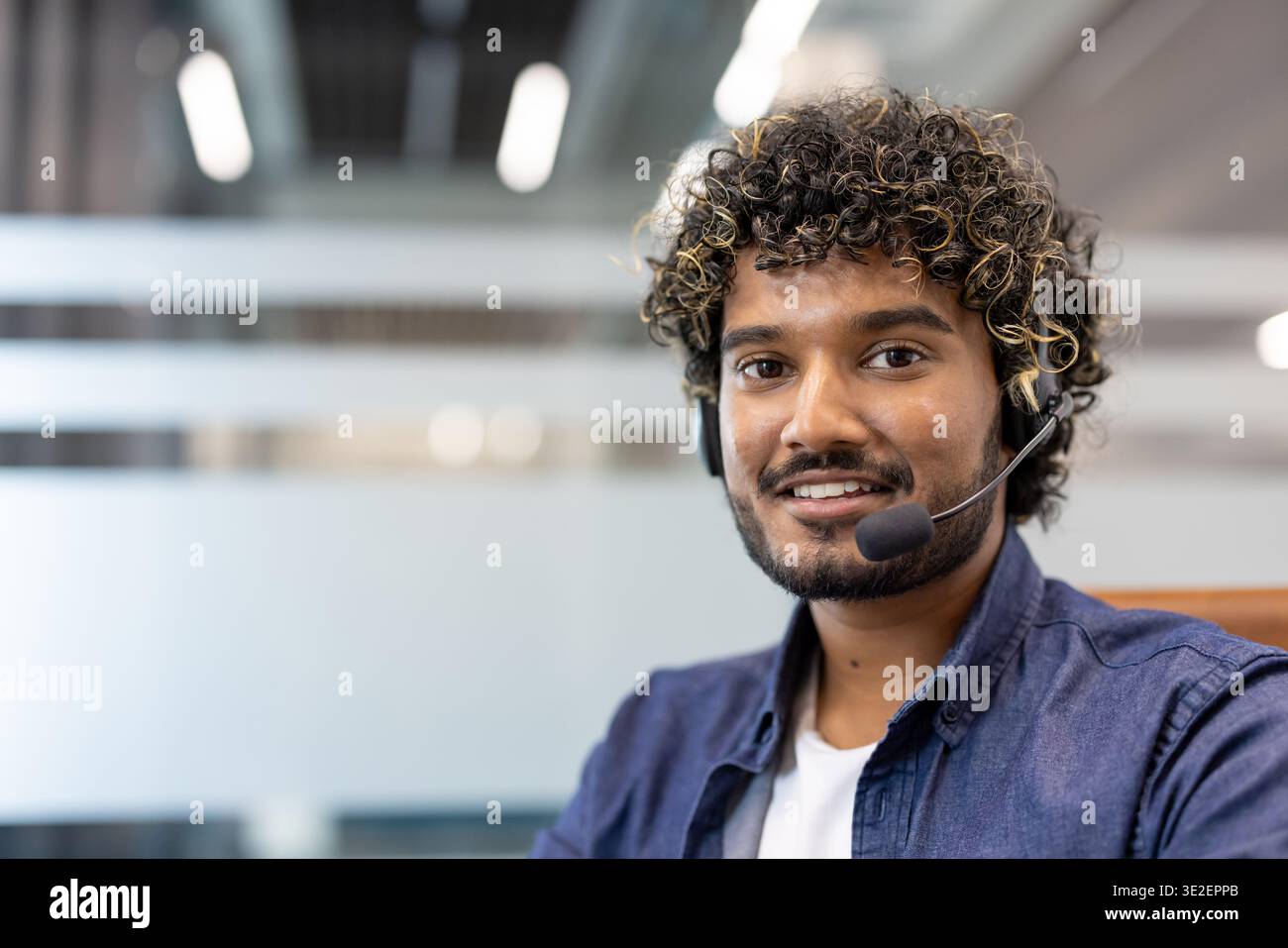 Nahaufnahme eines jungen Indianers in einem Headset, der im Büro steht und in die Kamera lächelt. Stockfoto