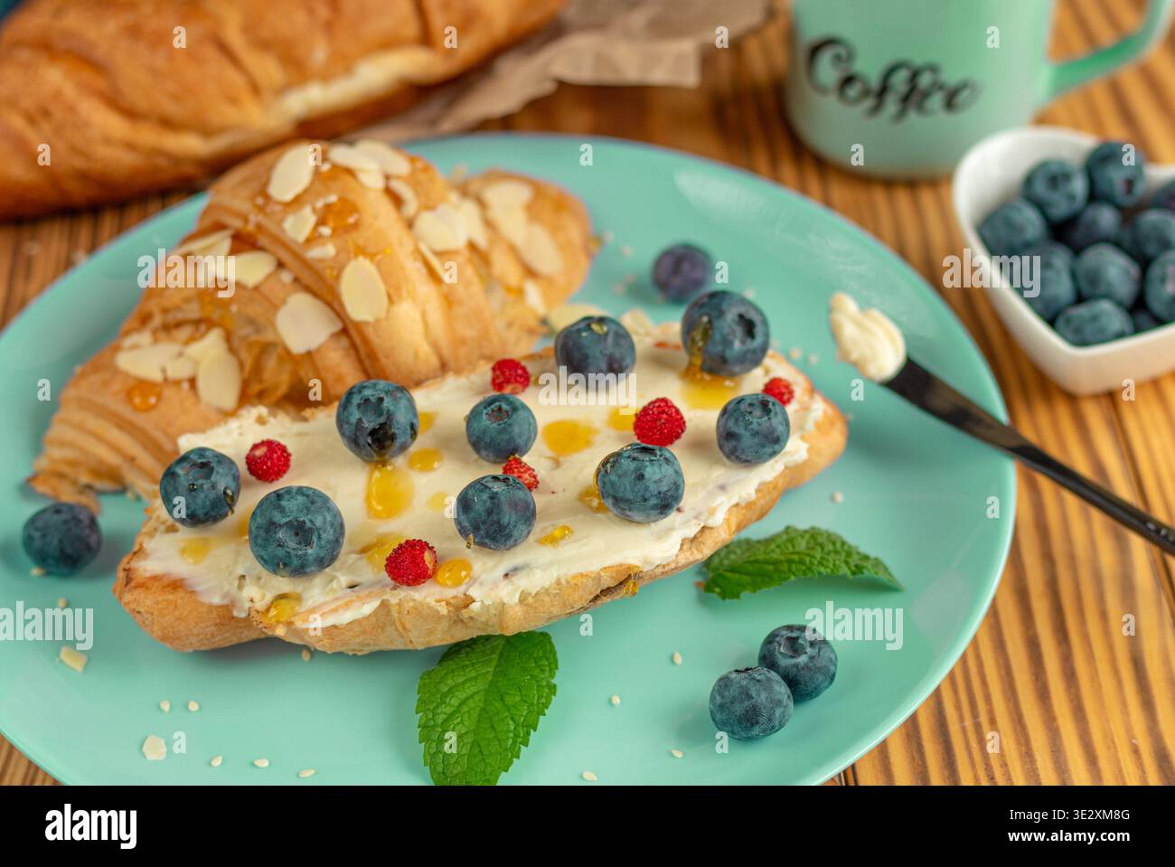 Frisches Croissant mit Cream Cheese, Heidelbeeren und Honig. Croissant-Füllungsidee Stockfoto