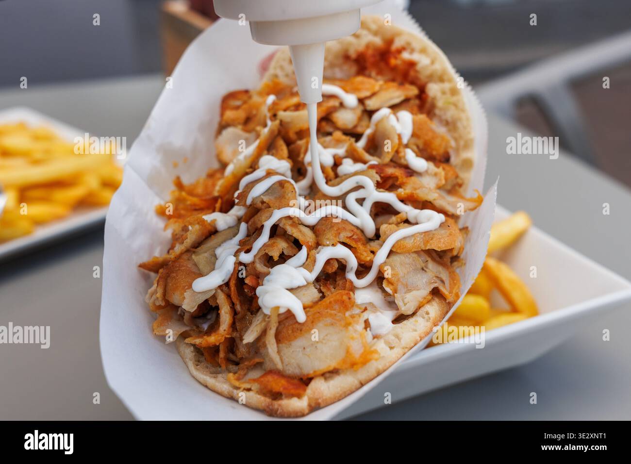 Nahaufnahme einer Squeeze-Flasche, in der weiße Soße über einen frisch zubereiteten Hühnerkebab gegossen wird Stockfoto