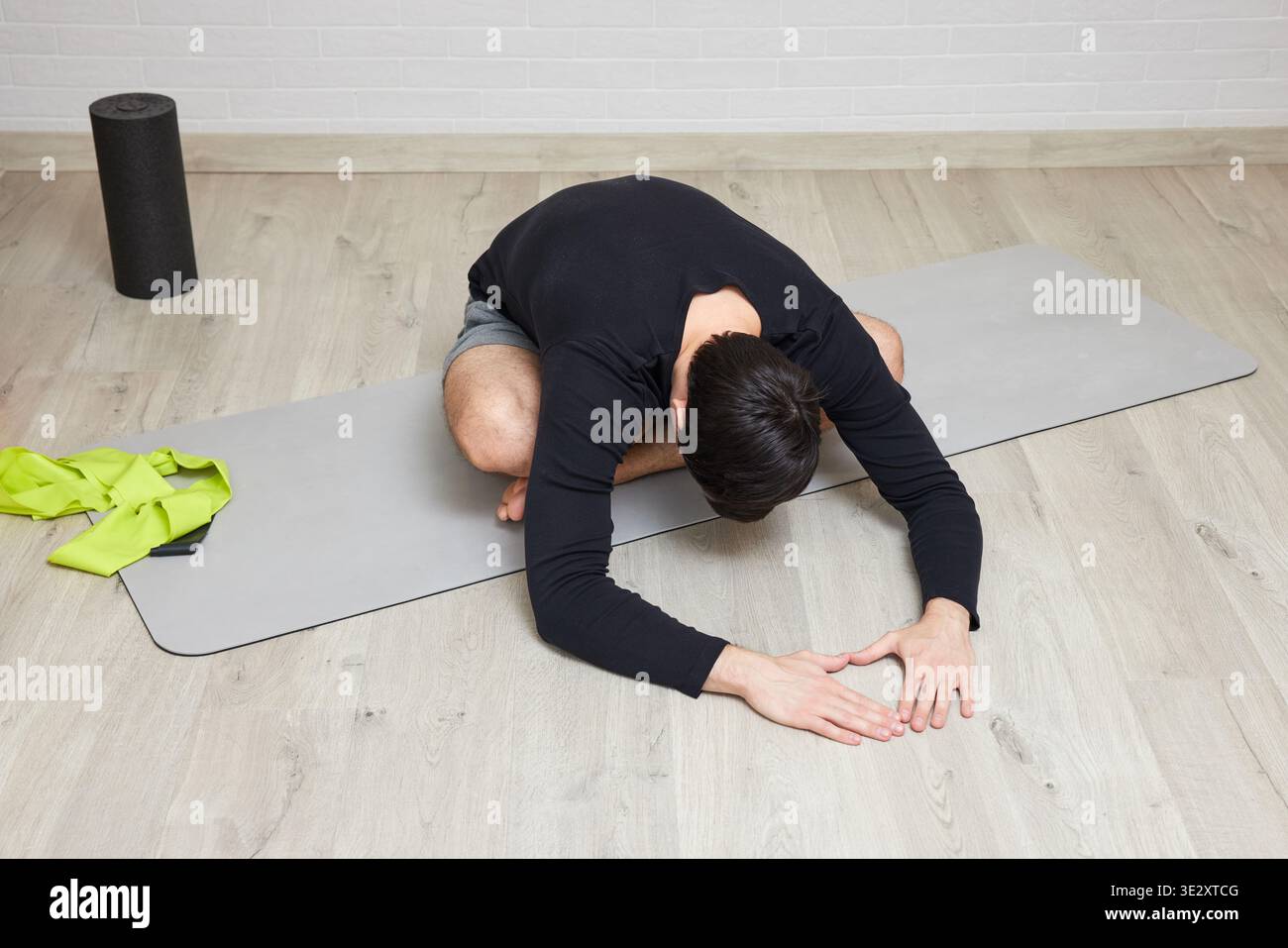 Ein Mann, der eine Yoga-Stretching-Pose auf einer Matte macht, mit einer Schaumrolle in der Nähe Stockfoto