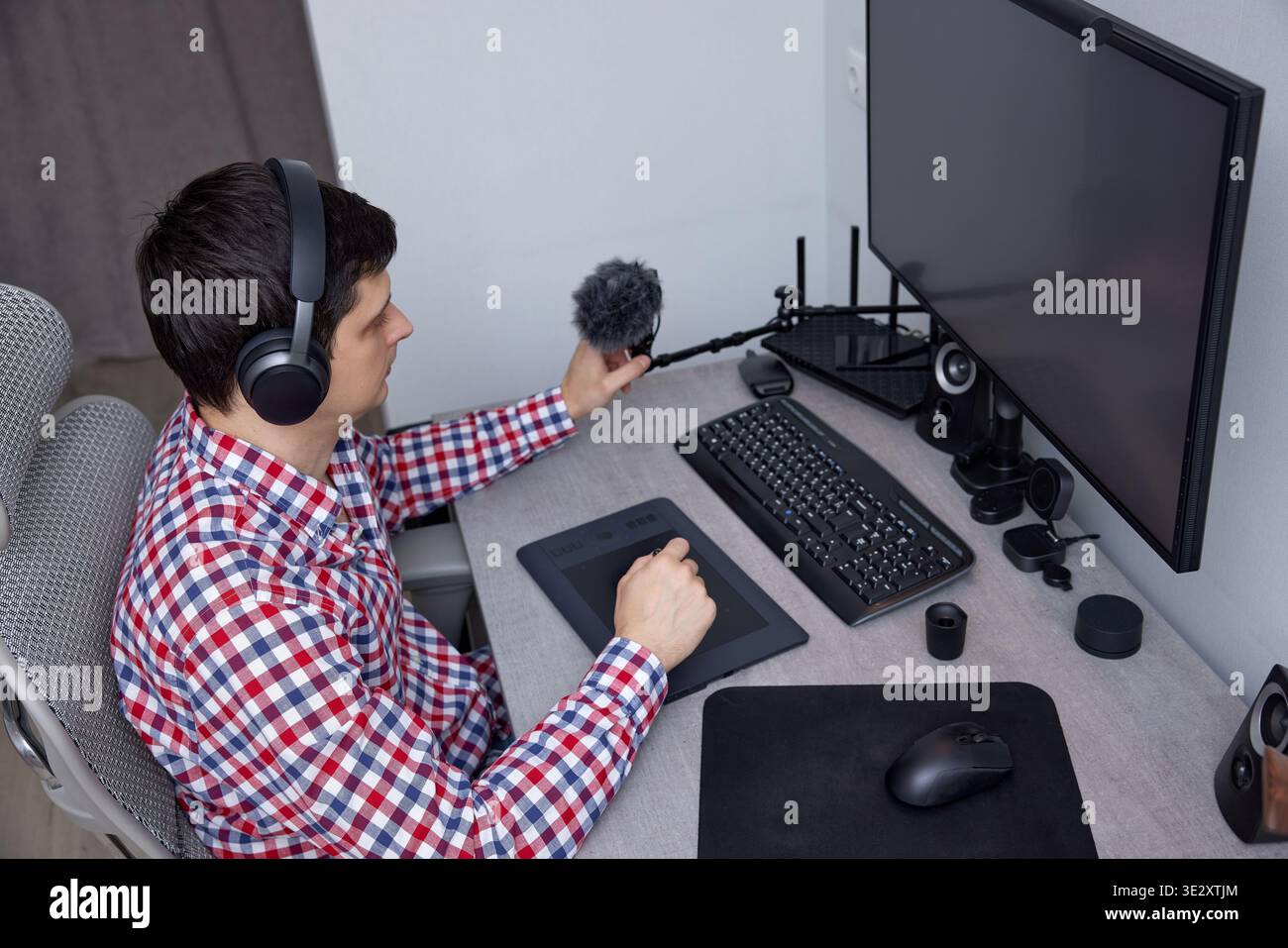 Mann, der Kopfhörer trägt und an seinem Schreibtisch ein Mikrofon und ein Grafiktablett verwendet Stockfoto