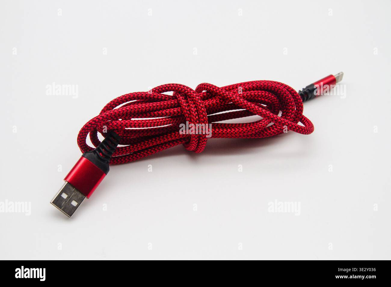 Smartphone-Ladekabel mit rotem und schwarzem Muster und Anschlusssteckern, zur Aufbewahrung aufgerollt und auf weißem Hintergrund Stockfoto
