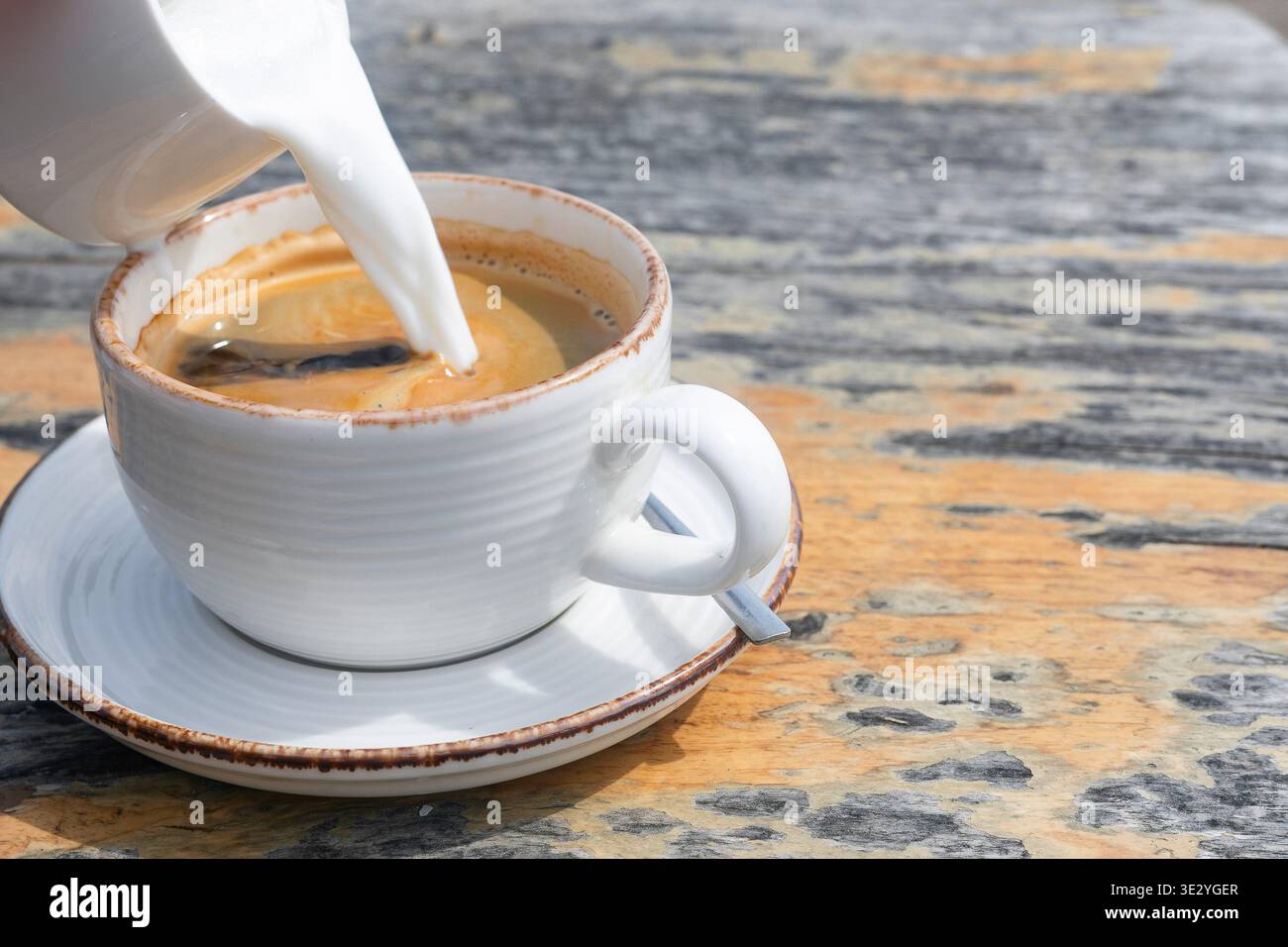 Milch in eine Tasse Americano auf rustikalem Holztisch gießen Stockfoto