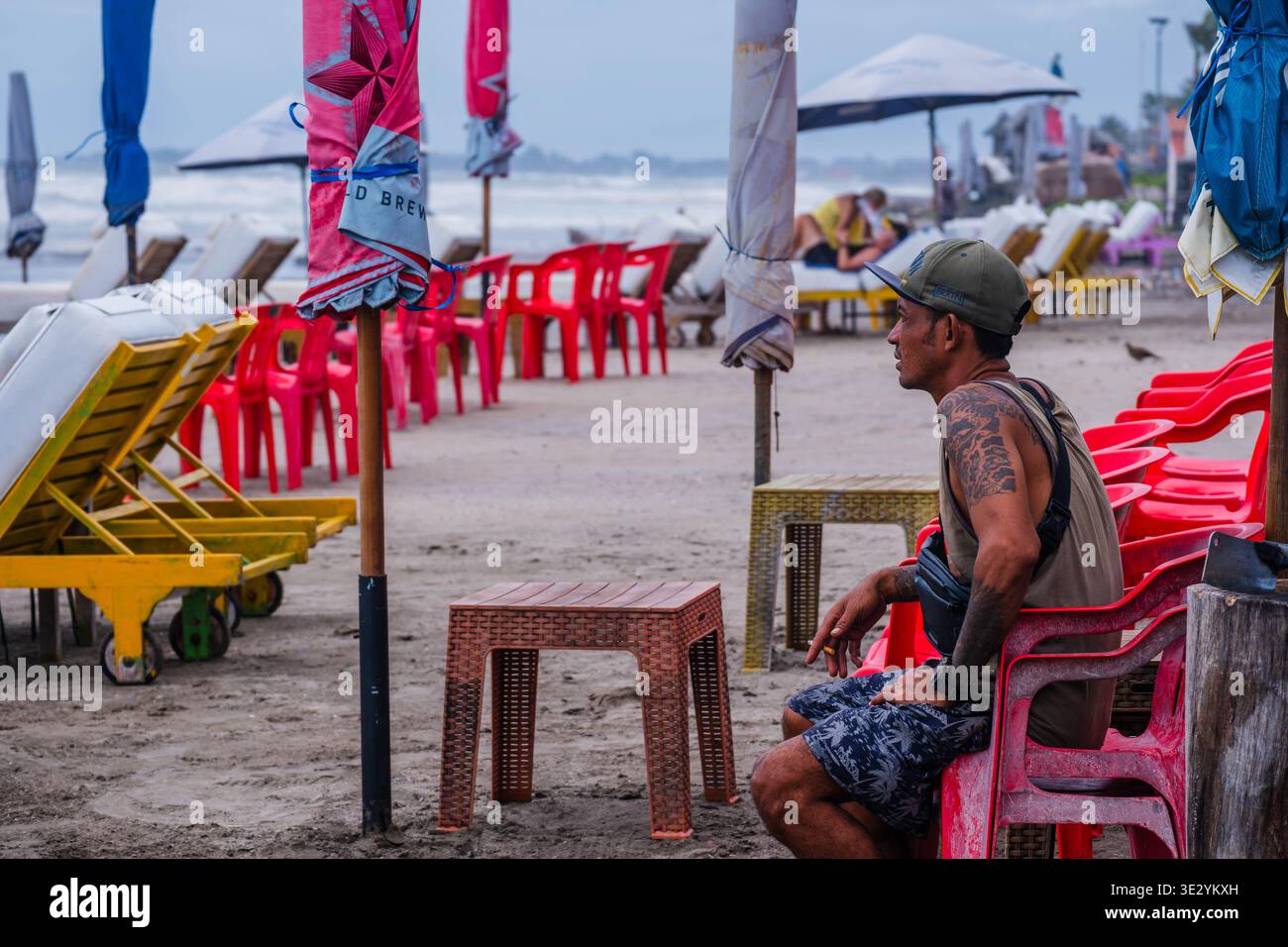 Tätowierter Mann sitzt auf einem Plastikstuhl am Strand Stockfoto
