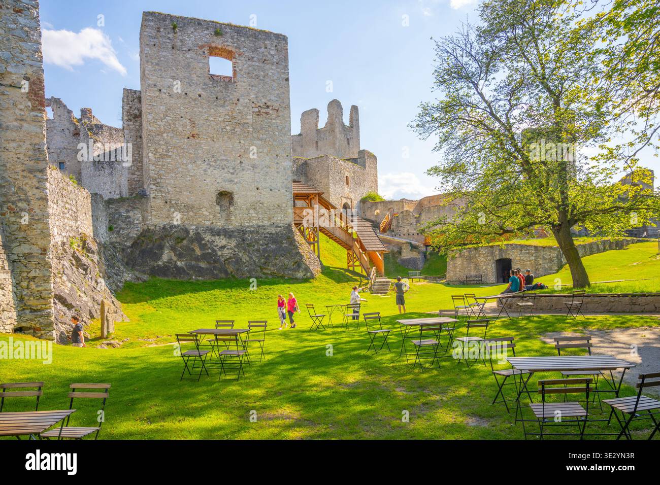 Besucher spazieren durch den Innenhof des Schlosses Rabi. Die Burgruine ist die größte in Böhmen. Grünes Gras und Steinmauern umgeben die Gegend und schaffen eine historische Umgebung. Stockfoto