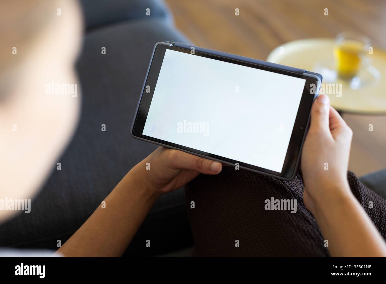 Vertikales Video: Sich niederlassende Frau in einem kurzärmligen Top-Tablet mit leerem weißen Bildschirm auf dem Sofa Stockfoto