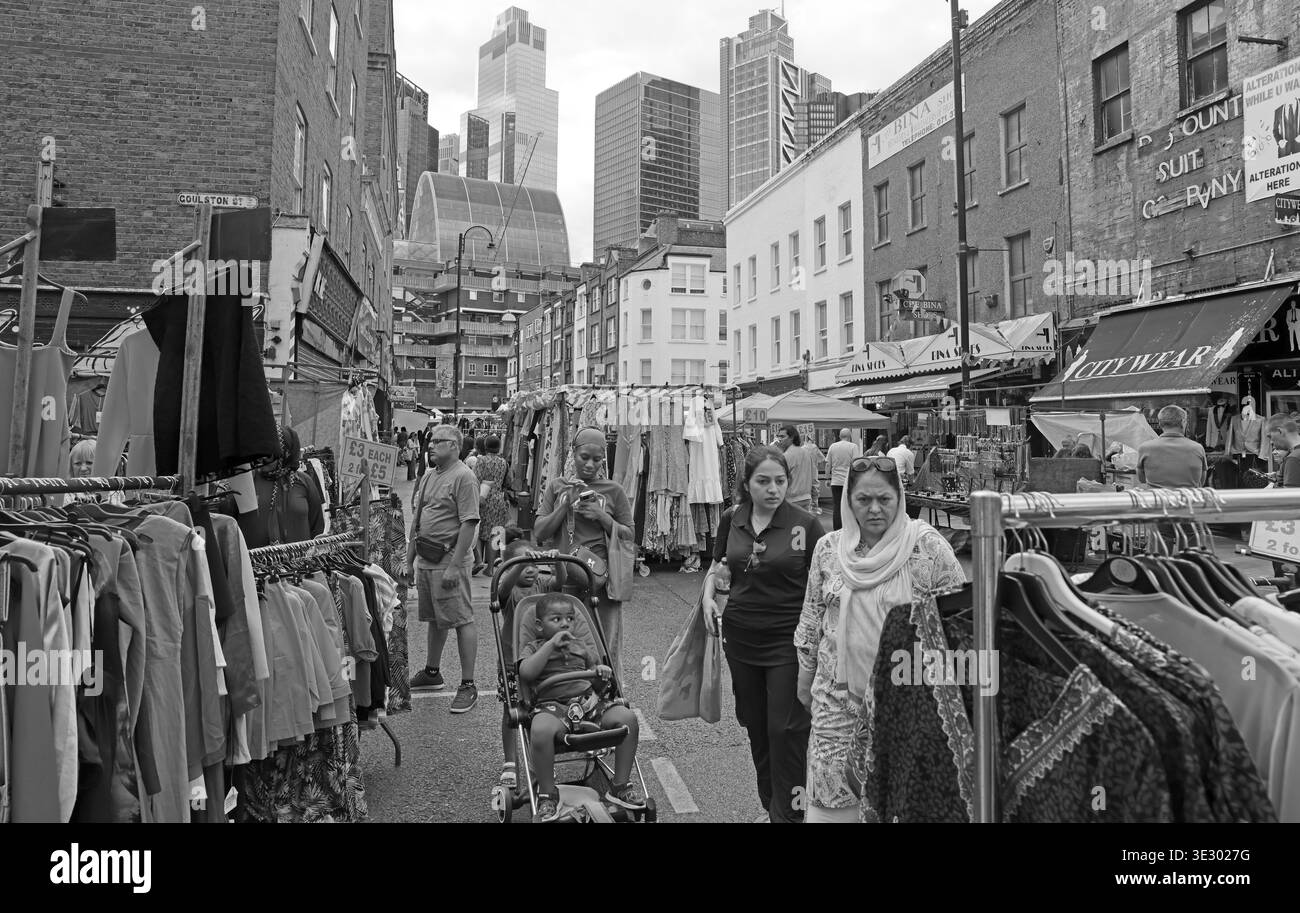 Straßenmarkt-Kleidungsstände in der 29 Wentworth Street im East End von London, mit der Skyline der City im Hintergrund. Stockfoto