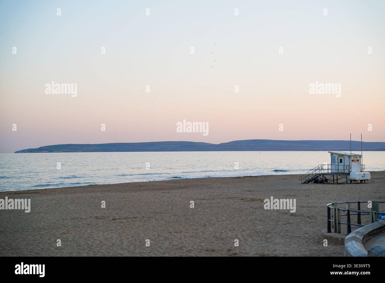 Leerer Bournemouth Beach in der Abenddämmerung mit Rettungsschwimmerturm, ruhigem Meer und pastellrosa Sonnenuntergangshimmel über der Küste von Dorset, England, Großbritannien Stockfoto