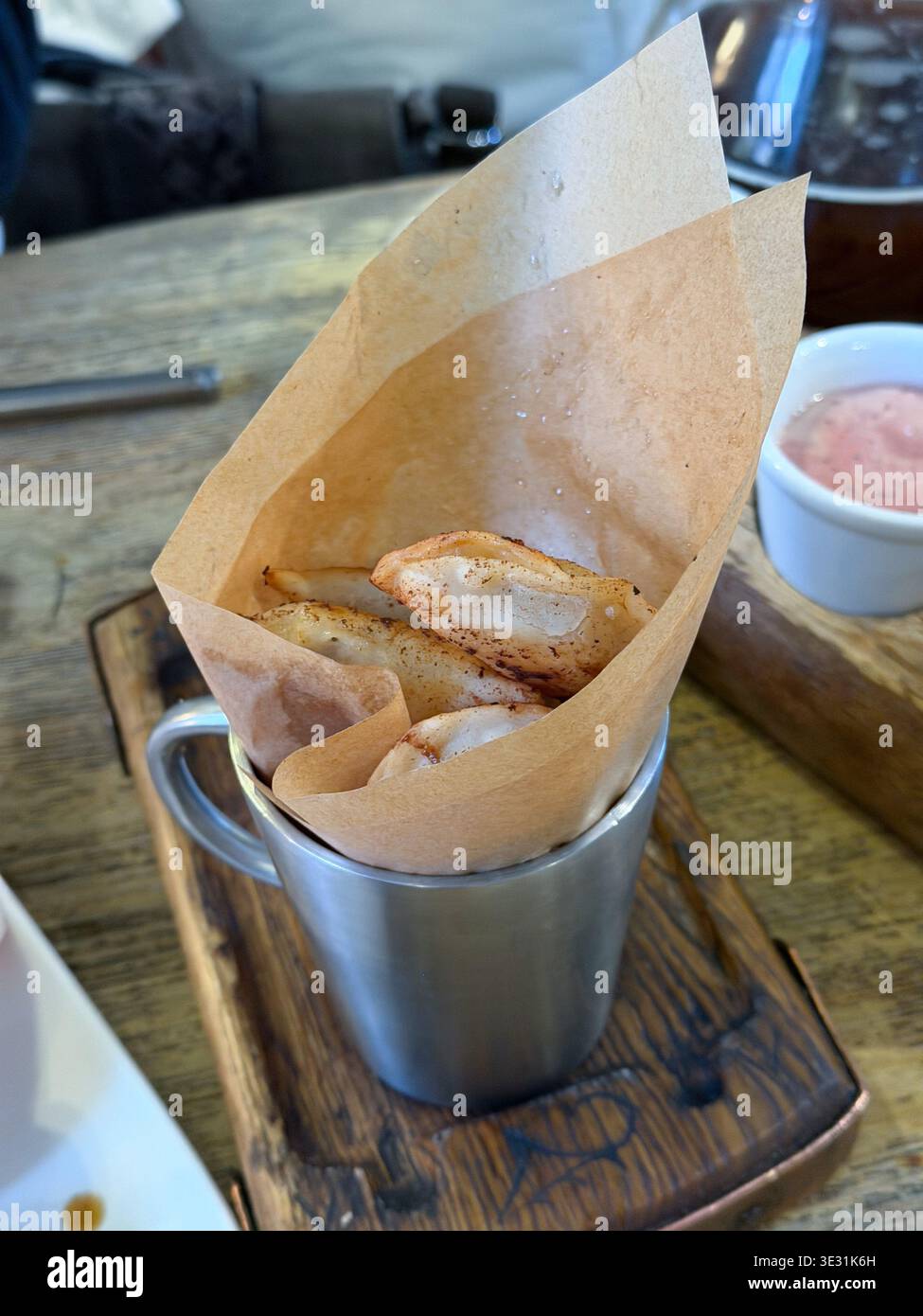 Gebratene Knödel in Metallbecher mit Papierfutter auf Holzbrett mit Soße im Hintergrund im Restaurant, knuspriger Snack mit goldener Oberfläche Stockfoto