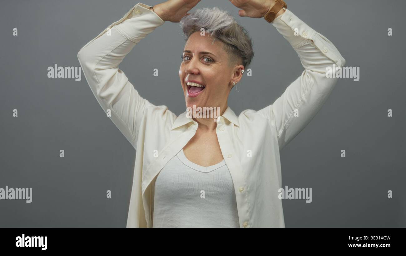 Weiße Frau macht Dachgesten mit Händen über Kopf in grauem Studio; Schutz Komfort Sicherheit Glück. Stockfoto